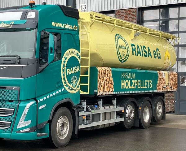 RAISA eG LKW mit gelbem Tank für Premium-Holzpellets steht vor einer Industriehalle auf nassem Boden.